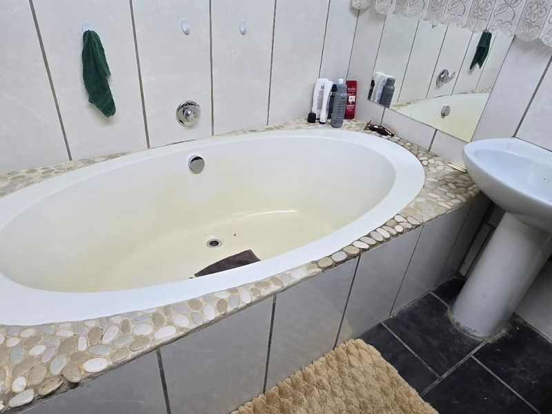 A bathroom featuring a built-in oval bathtub with a decorative pebble-style surround and a classic pedestal washbasin.