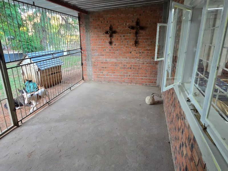 A covered outdoor patio area featuring exposed brick walls, concrete flooring, and secure metal gate enclosure overlooking the garden.
