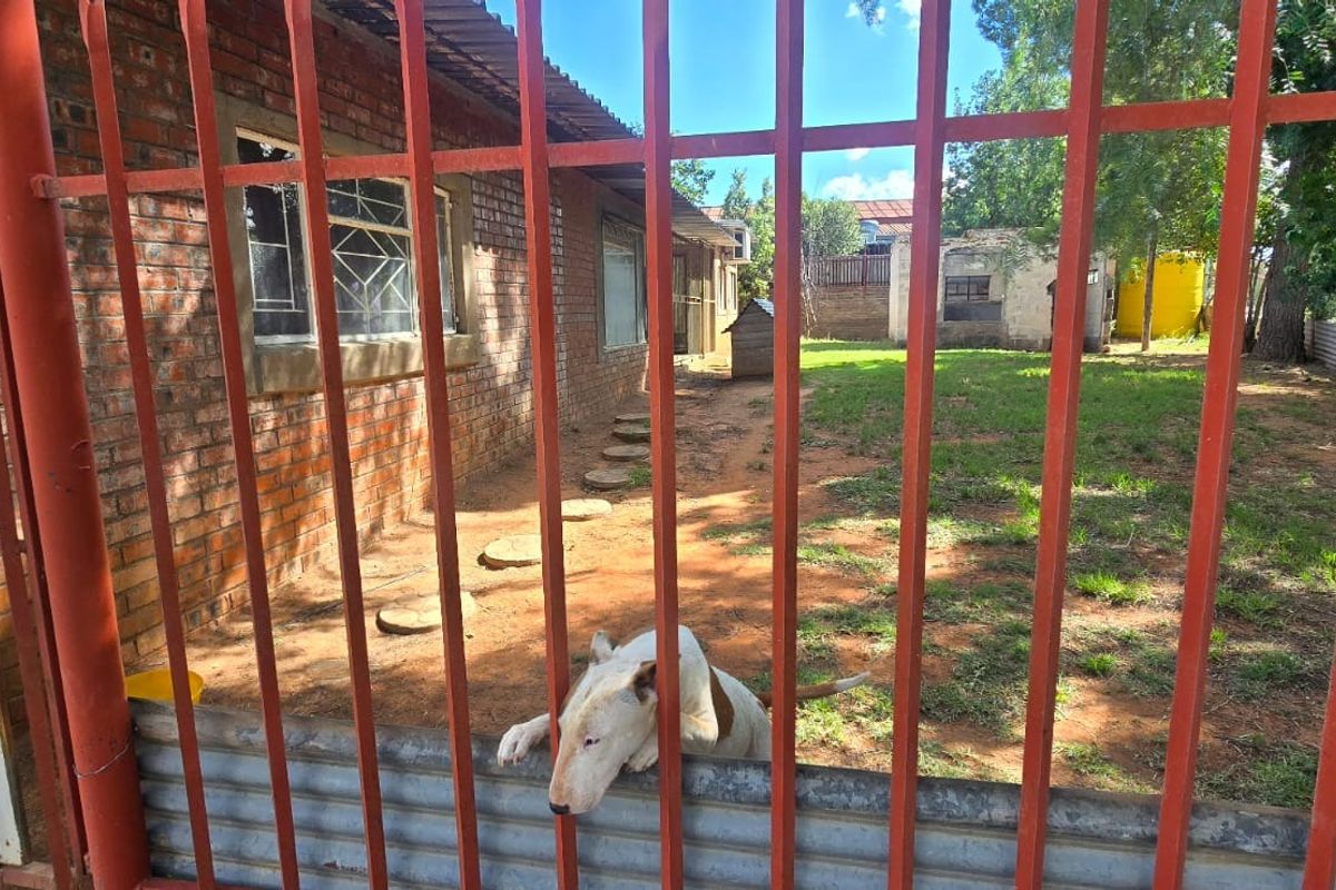 Rear exterior view of the industrial property featuring a brick facade, security fencing, and a spacious yard area.