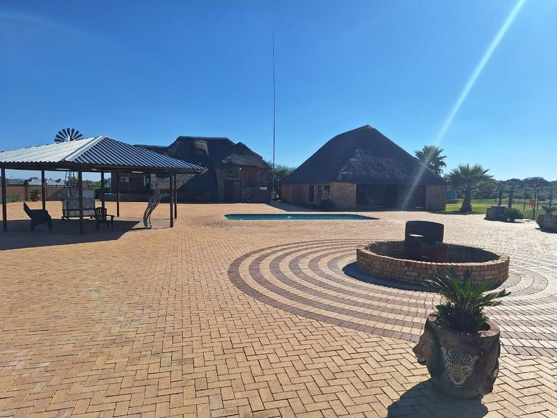 Spacious outdoor entertainment area featuring a large brick-paved courtyard, swimming pool, covered patio, and a traditional thatched-roof farmhouse structure.