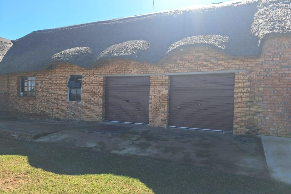 Exterior view of a farm-style building featuring a traditional thatched roof, face brick exterior, and two roller garage doors with a concrete driveway.