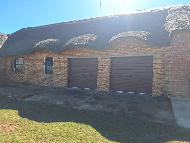 Exterior view of a farm-style building featuring a traditional thatched roof, face brick exterior, and two roller garage doors with a concrete driveway.