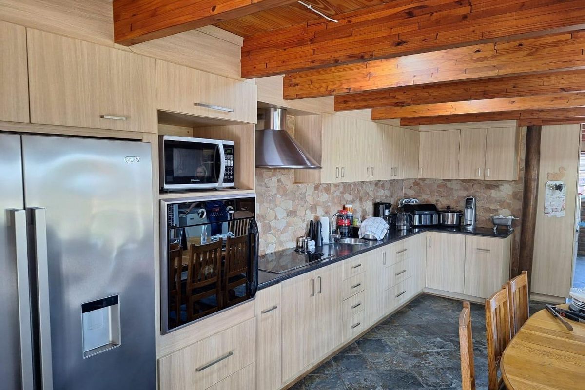 A well-maintained kitchen featuring light wood cabinetry, stone tile backsplash, exposed timber ceiling beams, and durable stone flooring.