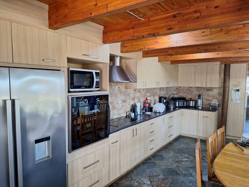 A well-maintained kitchen featuring light wood cabinetry, stone tile backsplash, exposed timber ceiling beams, and durable stone flooring.