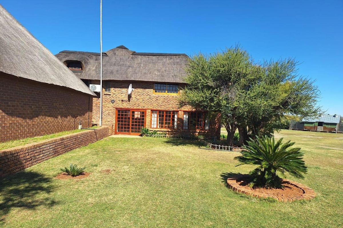 Rear view of a traditional face brick farmhouse featuring a classic thatch roof, timber-framed windows, and a well-maintained garden area.