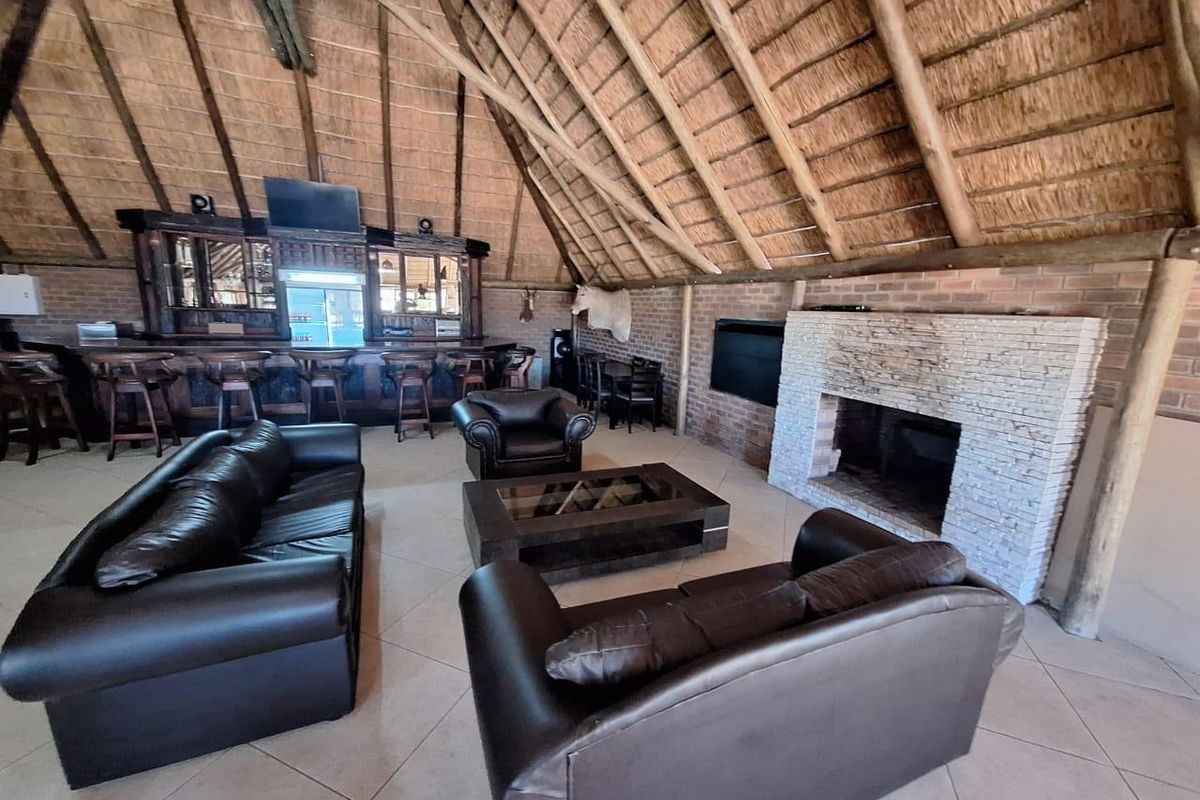 Spacious living area featuring a high thatched roof with exposed timber rafters, a brick fireplace, and a built-in bar area.