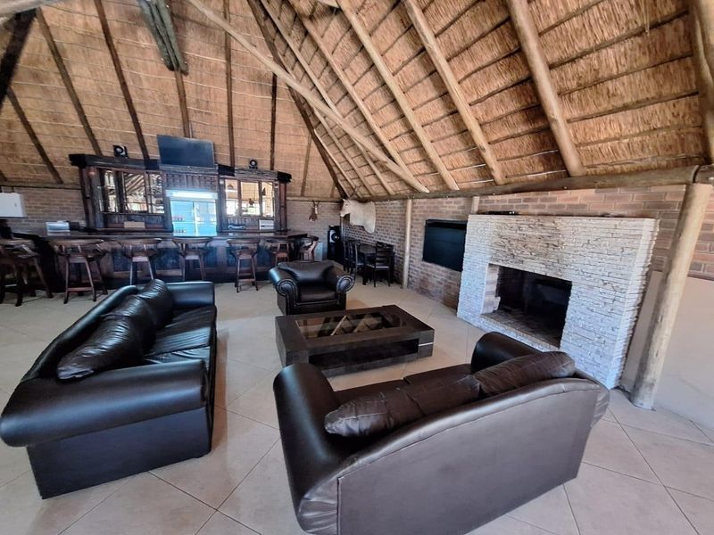 Spacious living area featuring a high thatched roof with exposed timber rafters, a brick fireplace, and a built-in bar area.