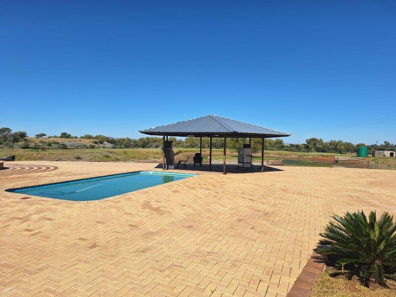 Spacious outdoor pool area featuring a large paved deck and a covered entertainment pavilion overlooking the surrounding farm landscape.