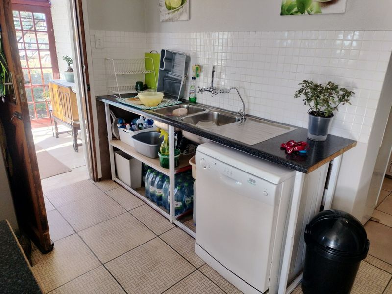 A functional scullery area featuring a double bowl stainless steel sink, tiled backsplash, and space for a dishwasher with tiled flooring.
