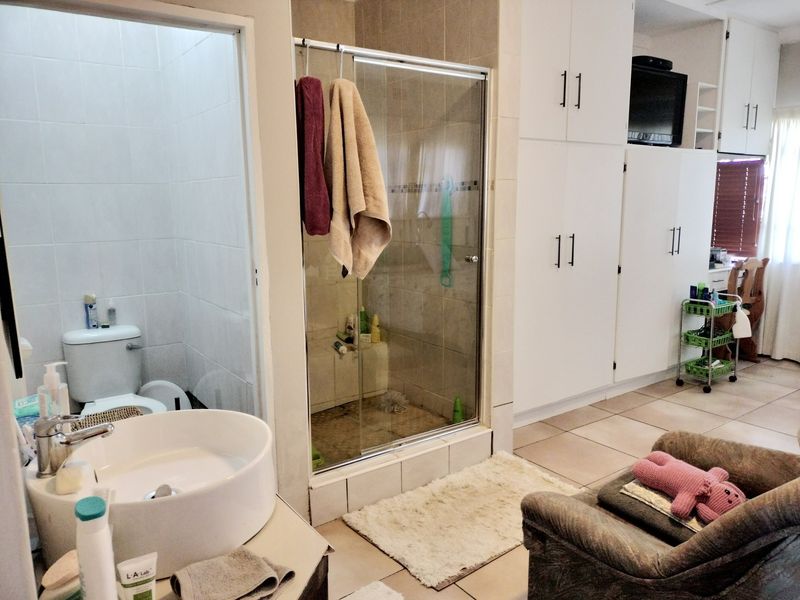 A functional bathroom featuring a glass-enclosed shower, built-in storage cabinetry, and a modern vessel sink, with tiled flooring throughout.