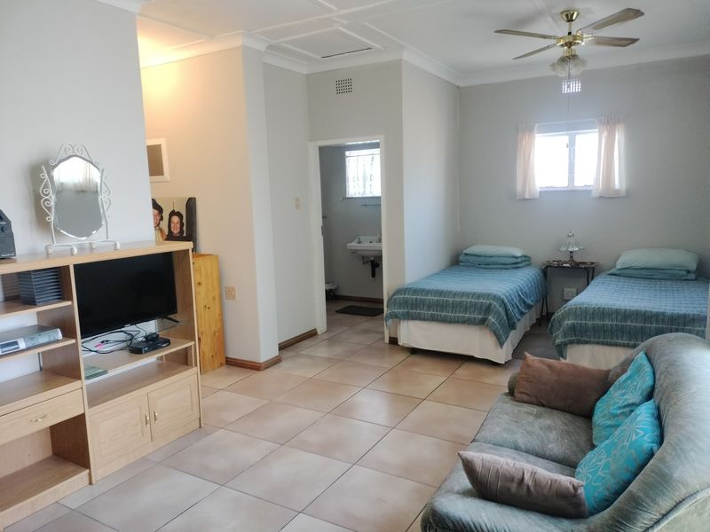 Spacious bedroom featuring tiled flooring, a ceiling fan, and an en-suite washbasin area, offering a functional layout with neutral wall finishes.