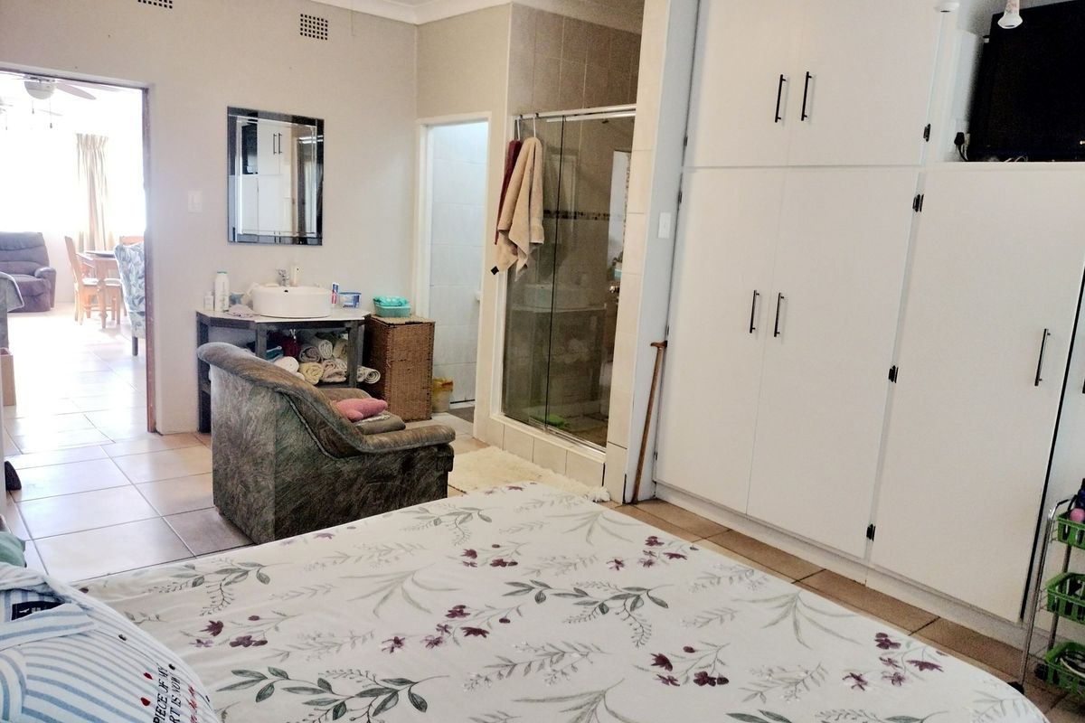 Spacious bedroom featuring built-in cupboards, an en-suite shower, and a vanity basin area with tiled flooring.