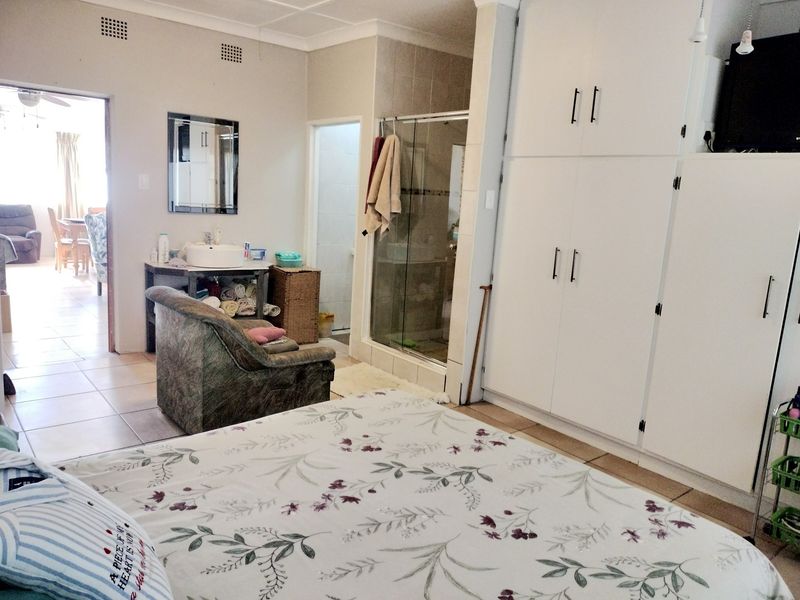 Spacious bedroom featuring built-in cupboards, an en-suite shower, and a vanity basin area with tiled flooring.