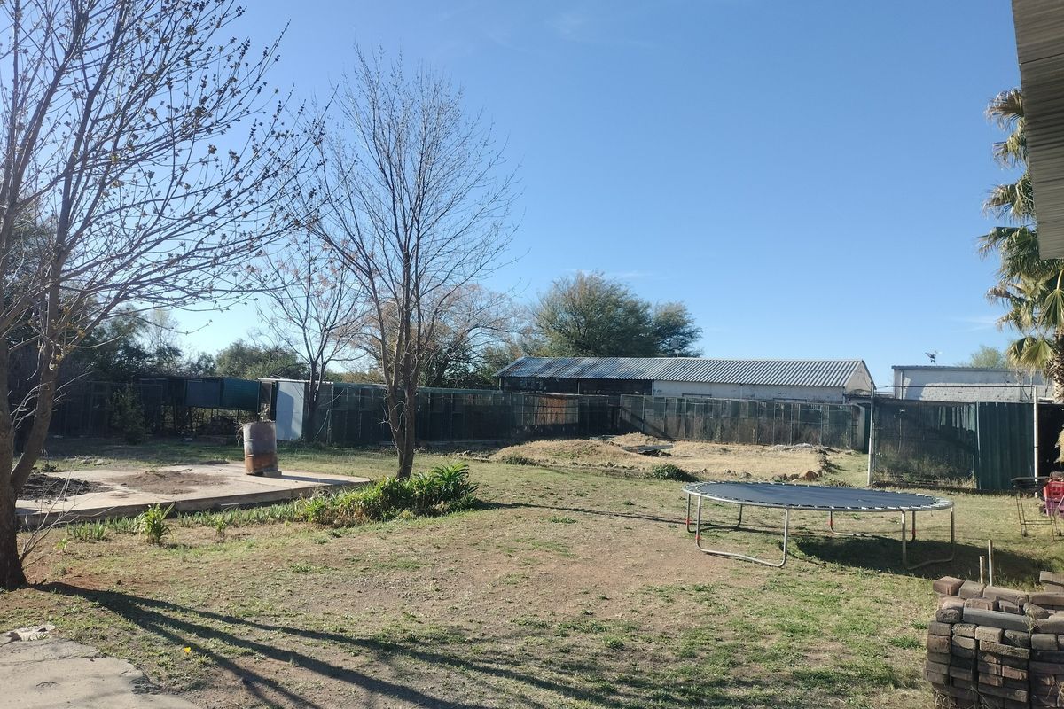 Spacious rear yard area featuring metal perimeter fencing, a concrete slab, and a large industrial-style structure with a corrugated metal roof.