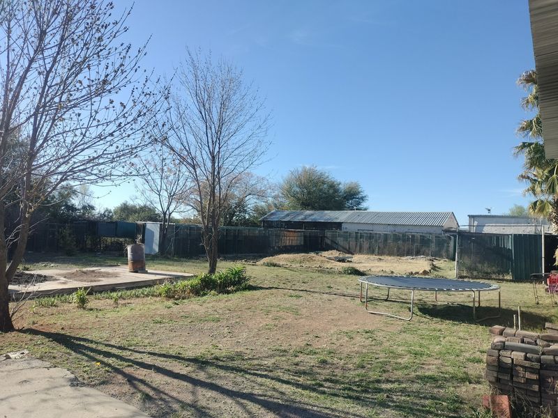 Spacious rear yard area featuring metal perimeter fencing, a concrete slab, and a large industrial-style structure with a corrugated metal roof.