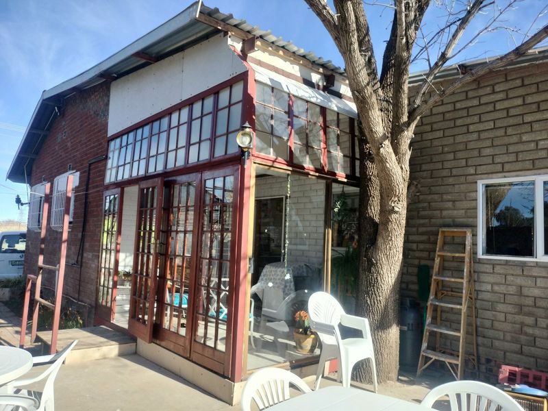 Rear exterior view of an industrial-style building featuring a timber-framed glass sunroom, brick facade, and concrete patio area.