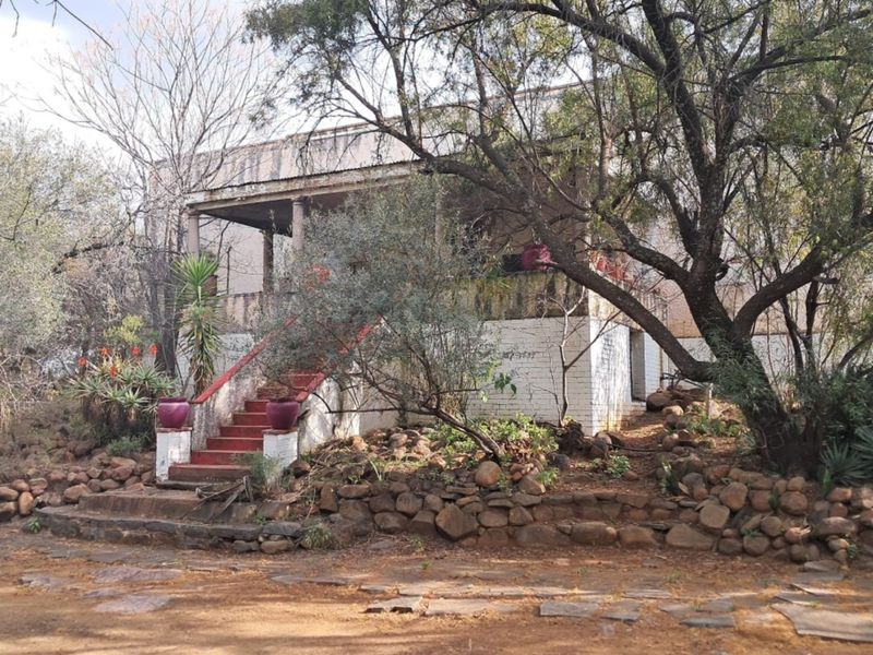 Front view of a farm property featuring a raised covered veranda, stone retaining walls, and a concrete staircase leading to the main entrance.