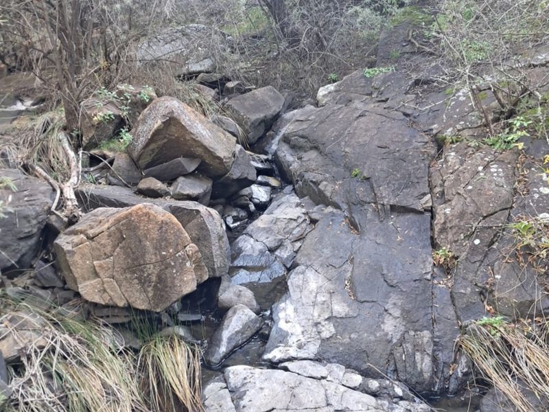 A natural landscape view featuring rugged rock formations and a small seasonal stream bed on the farm property.