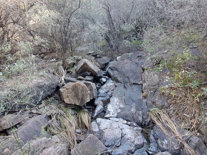 A natural landscape view featuring rocky terrain and a small stream running through the farm property.