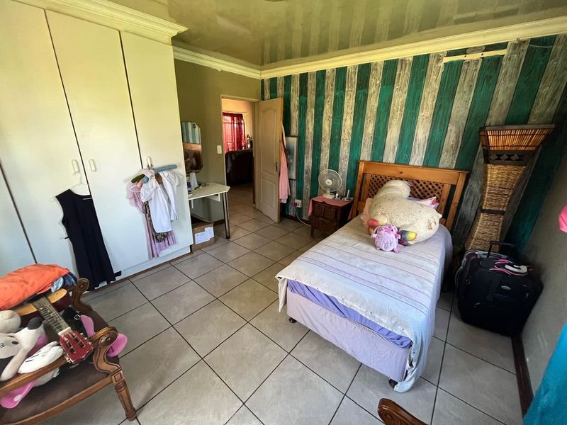 A bedroom featuring tiled flooring, built-in cupboards, and decorative wall finishes, offering a functional space that could benefit from cosmetic updates.