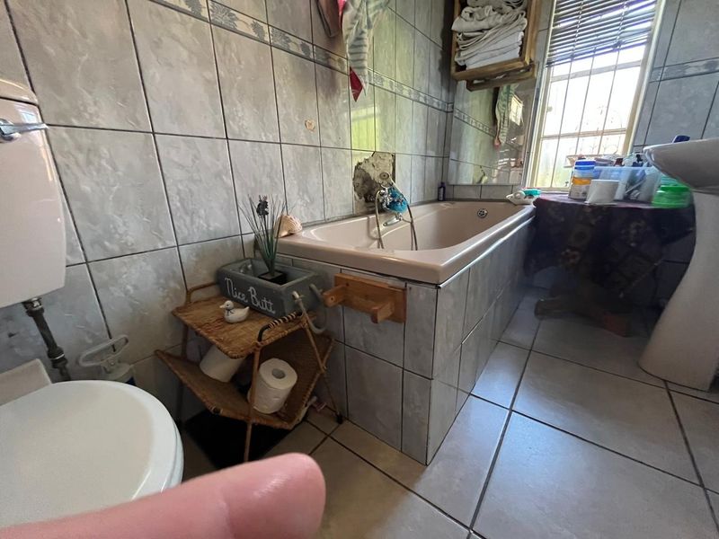 A dated bathroom featuring a bathtub, pedestal basin, and toilet, with visible damage to the wall tiling behind the bathtub area.