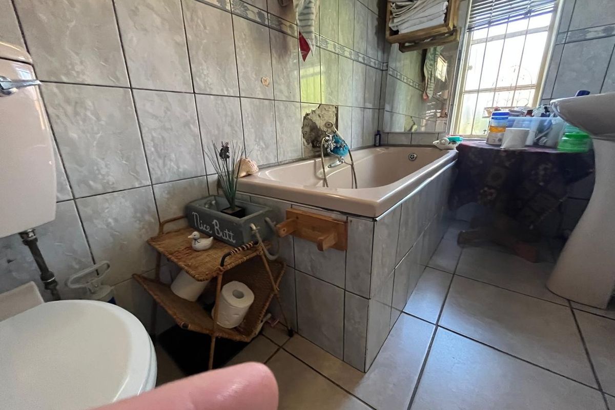 A dated bathroom featuring a bathtub, pedestal basin, and toilet, with visible damage to the wall tiling behind the bathtub area.