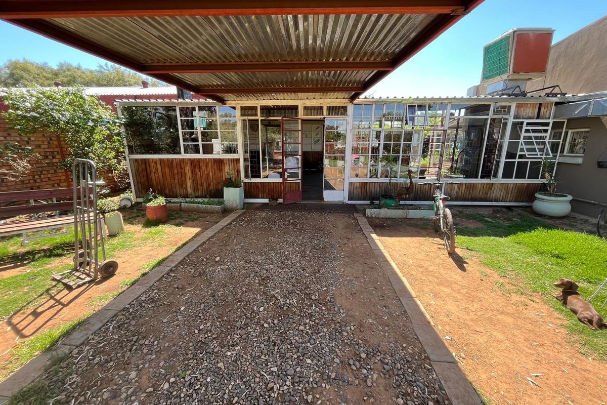 Rear exterior view featuring a covered patio area with corrugated metal roofing, timber wall cladding, and extensive steel-framed glazing.