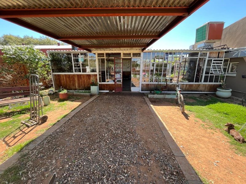 Rear exterior view featuring a covered patio area with corrugated metal roofing, timber wall cladding, and extensive steel-framed glazing.