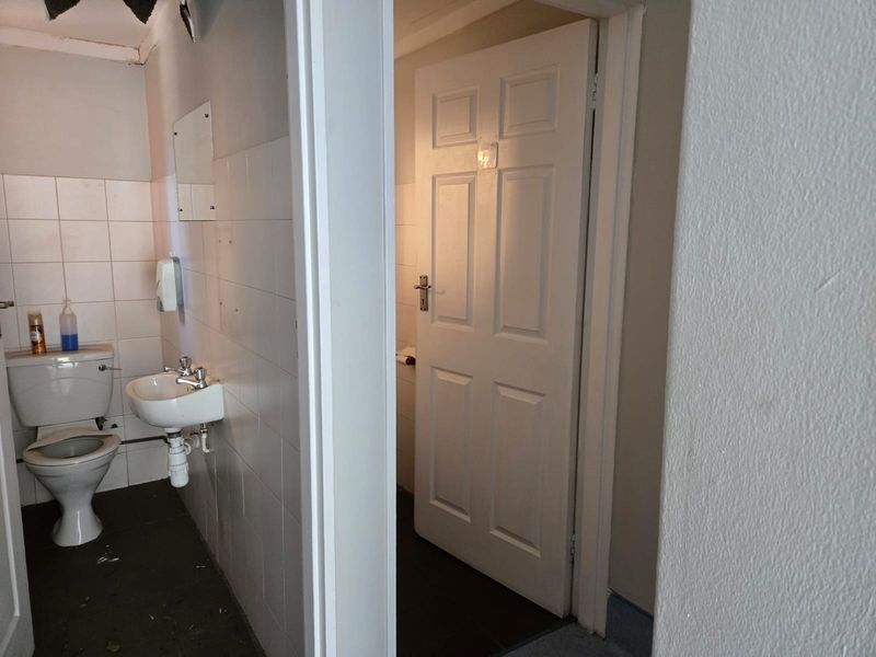 A functional commercial bathroom featuring a wall-mounted basin, toilet, and tiled walls, requiring some maintenance and cosmetic updates.