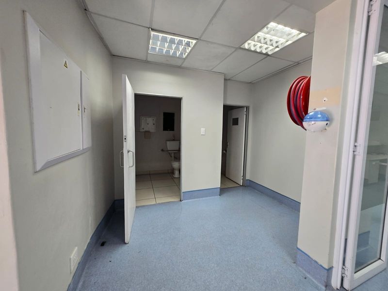 A functional commercial utility space featuring vinyl flooring, suspended ceiling with recessed lighting, and access to an adjacent restroom facility.