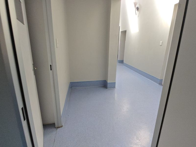A clean, empty commercial hallway featuring durable vinyl flooring and neutral wall finishes, providing access to multiple internal rooms.
