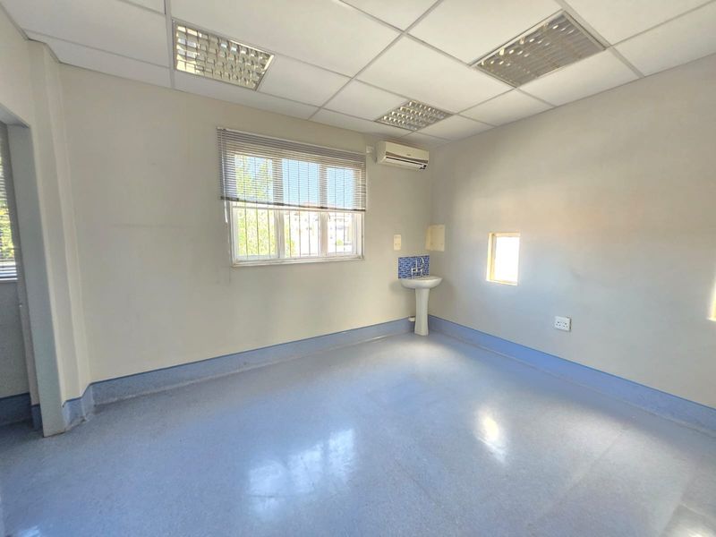 A functional, empty commercial office space featuring a pedestal basin, suspended ceiling, air conditioning, and durable vinyl flooring.
