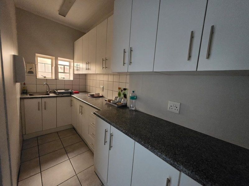 A functional scullery featuring white cabinetry, granite countertops, a stainless steel sink, and tiled flooring, providing ample storage and workspace.