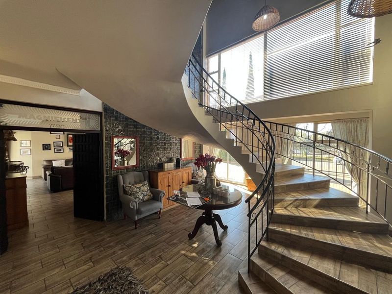 Grand entrance hall featuring a striking curved staircase with wrought iron balustrade, large windows, and decorative feature wall tiling.