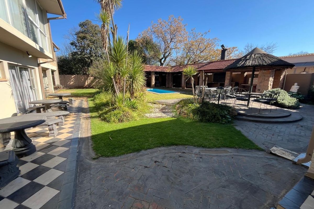 Spacious rear garden featuring a swimming pool, a thatched lapa with built-in braai, and extensive paved patio areas suitable for outdoor entertaining.