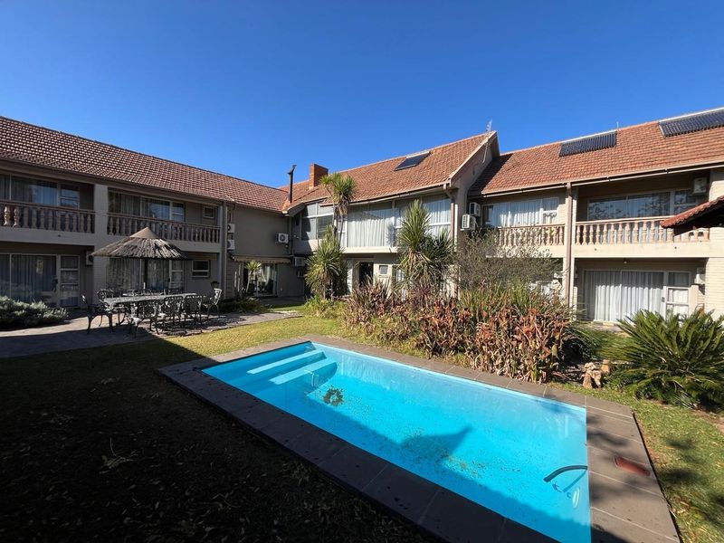 A rear courtyard view of a guest house featuring a swimming pool, paved patio, and multi-level balconies with solar water heating panels on the roof.