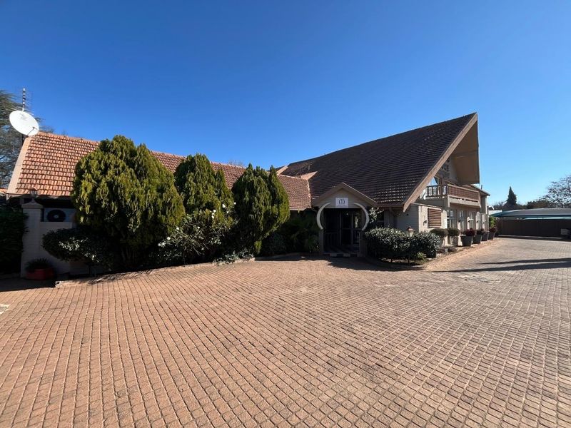 Front exterior view of the guest house featuring a large paved driveway, traditional tiled roof architecture, and a prominent entrance.