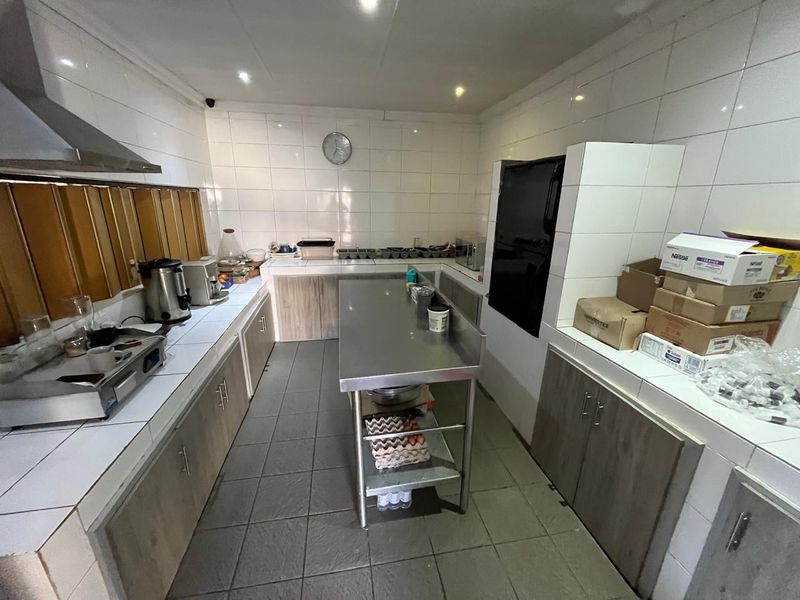 A functional commercial-style kitchen featuring tiled surfaces, stainless steel prep counters, built-in cabinetry, and an extractor fan, suitable for guest house operations.