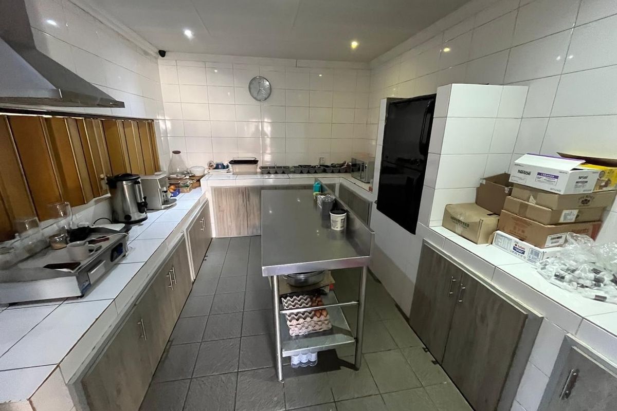 A functional commercial-style kitchen featuring tiled surfaces, stainless steel prep counters, built-in cabinetry, and an extractor fan, suitable for guest house operations.