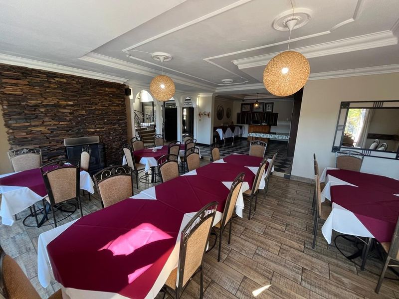 Spacious dining area featuring a prominent stone feature wall with a built-in fireplace, decorative ceiling moldings, and durable tiled flooring throughout.