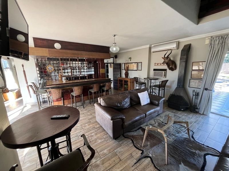 A spacious bar area featuring a built-in counter, glass shelving, tiled flooring, and a fireplace, with direct access to the outdoor patio area.