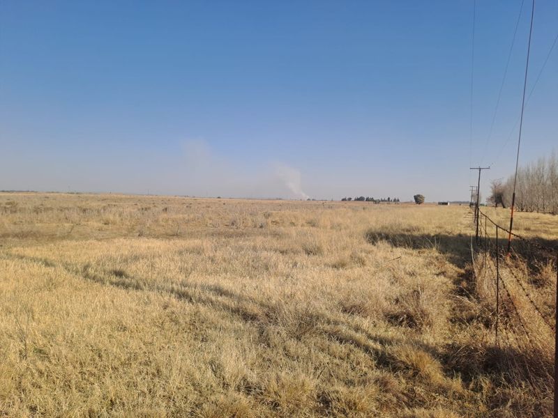 Expansive open farmland landscape featuring dry grass, utility poles, and a perimeter barbed wire fence.
