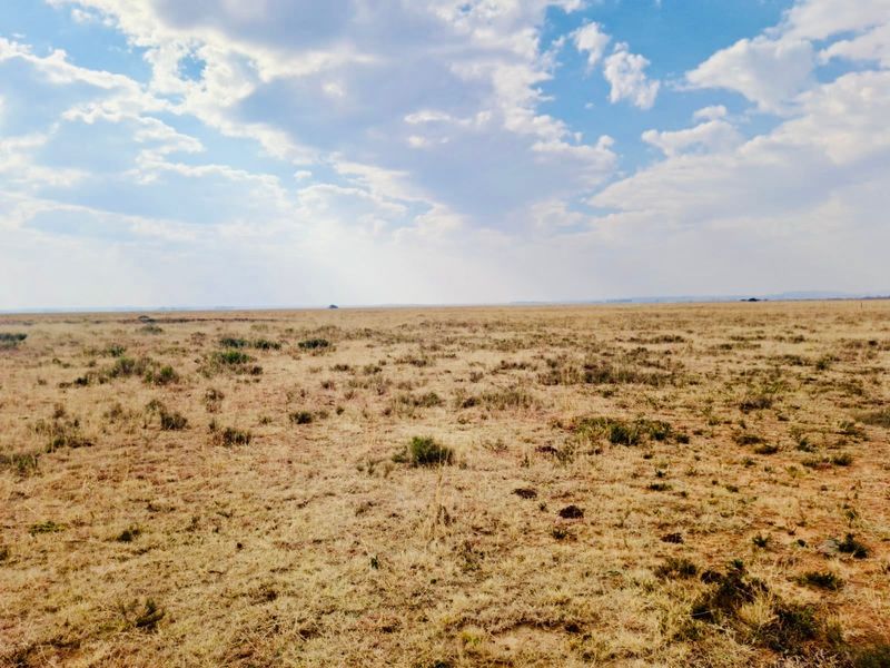 Expansive view of open farm land and natural veld under a cloudy sky.