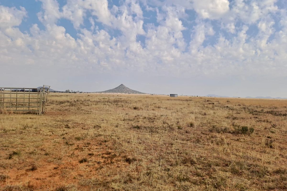 Expansive open farm landscape featuring natural terrain, distant mountain views, metal livestock fencing, and a water storage tank.