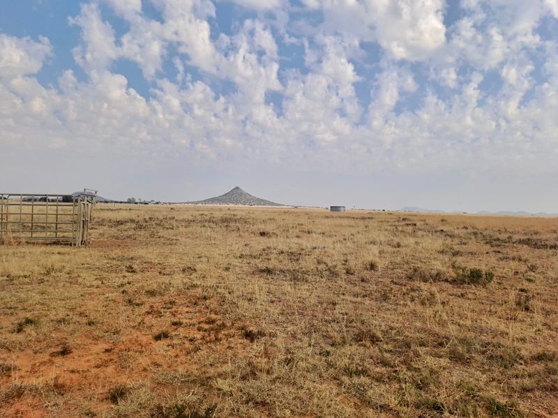 Expansive open farm landscape featuring natural terrain, distant mountain views, metal livestock fencing, and a water storage tank.