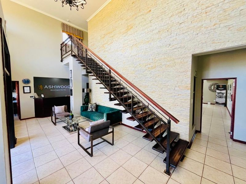 Spacious hotel lobby featuring a striking stone feature wall, an open-riser staircase with metal railings, and a dedicated reception area with tiled flooring.