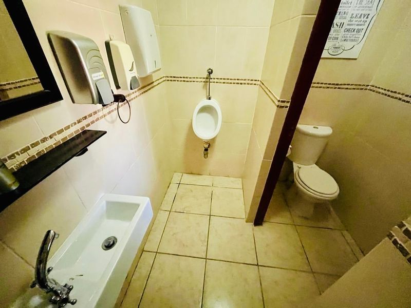 A functional guest house bathroom featuring a wall-mounted urinal, a standard flush toilet, and a wall-mounted basin with tiled finishes.