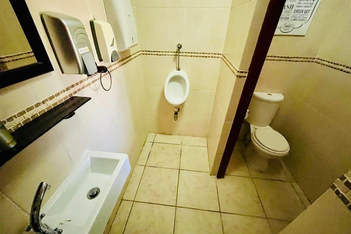 A functional guest house bathroom featuring a wall-mounted urinal, a standard flush toilet, and a wall-mounted basin with tiled finishes.
