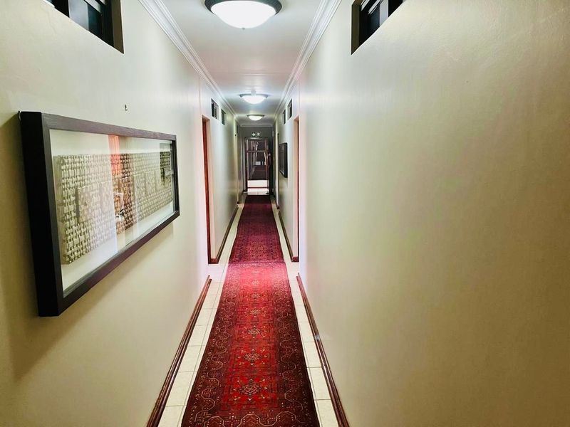 A well-maintained interior hallway featuring tiled flooring, ceiling cornices, and flush mount lighting, providing access to multiple rooms within the guest house.