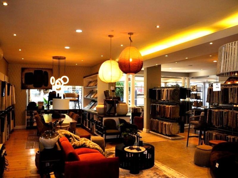 Spacious open-plan showroom featuring warm ambient lighting, recessed downlights, hardwood flooring, and extensive built-in display shelving for fabric samples.